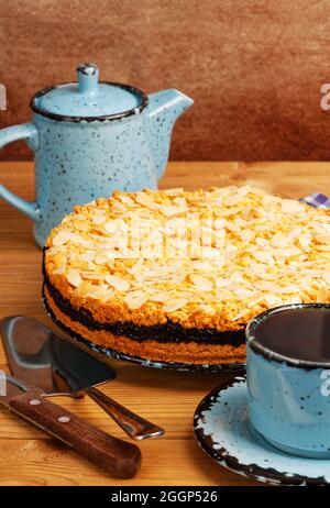Torta fatta in casa con ribes nero decorata con petali di mandorle e tazza di tè su tavolo di legno. Foto Stock