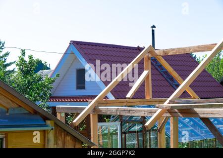 Tetti di case in legno e serre nel villaggio sullo sfondo del cielo blu e verde fogliame. Caldo sole giorno estivo. Piano medio Foto Stock