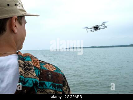 Giovane uomo che opera il drone di fotografia aerea su una piccola barca Foto Stock