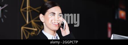 l'addetta alla reception era felice di sorridere e parlare con lo smartphone nella hall dell'hotel, con il banner Foto Stock