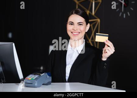 buon amministratore che detiene la carta di credito vicino al terminale di pagamento in hotel Foto Stock
