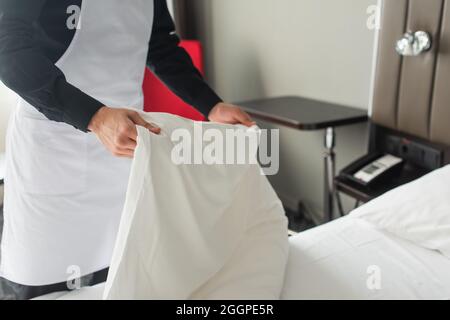 vista parziale della governante in grembiule che cambia biancheria da letto in camera d'hotel Foto Stock