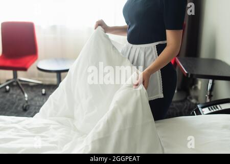 la camera d'hotel offre una vista parziale della cameriera giovane in un letto che cambia in modo uniforme Foto Stock