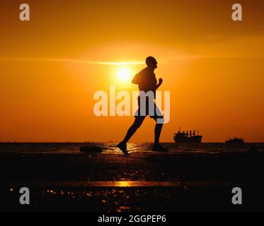 Silhouette di uomo che corre lungo la strada durante il tramonto. Foto Stock