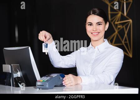 buona receptionist che tiene la chiave della camera vicino al lettore di carte di credito sul banco Foto Stock