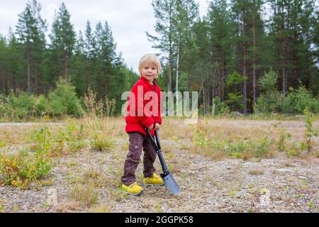 Bambino carino, scavando un buco, pulendo dopo se stesso su un campeggio selvaggio nella foresta Foto Stock