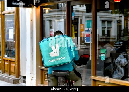 Londra, Inghilterra - agosto 2021: Persona che lavora per Deliveroo in attesa fuori da un ristorante da asporto per un ordine da consegnare Foto Stock