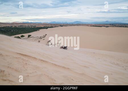 Vista pittoresca della moto parcheggiata su dune sabbiose nel deserto. Giorno di sole durante le vacanze estive. Dune di sabbia. Moto nel deserto. Foto Stock