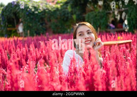 Felice bella giovane donna asiatica seduta in giardino di fiori cockpettine Foto Stock