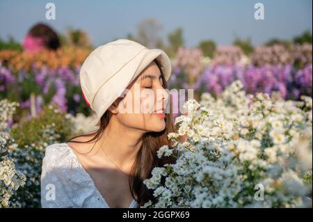 Bella giovane donna asiatica che indossa cappello odore taglierina fiore fioritura in giardino Foto Stock