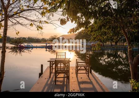 Suphanburi, Thailandia - Jan 18 2021 : tavolo in bambù Weave e sedie sul molo con vista sul lago di montagna in campeggio al tramonto Foto Stock