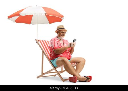 Uomo anziano seduto su una sedia da spiaggia e utilizzando uno smartphone sotto ombrello isolato su sfondo bianco Foto Stock