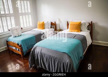 Una camera da letto con due letti singoli con copriletto color turchese e grigio e cuscini decorativi gialli Foto Stock