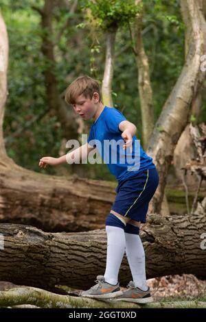 Ragazzo giovane che sale, clambering, bilanciamento su un tronco caduto di albero in bosco. Trovare e auto fiducia scoperta. Attività rurale e uno sfidi Foto Stock