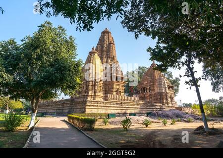 Vecchio tempio indù, costruito da Chandela Rajputs, nel sito occidentale in India Khajuraho incorniciata da alberi. Grigio bianco per la struttura beige più giovane e più vecchia Foto Stock