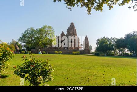 Vecchio e giovane tempio indù, costruito da Chandela Rajputs, presso il sito occidentale in India Khajuraho incorniciata da alberi. Grigio bianco per i più giovani e anziani Foto Stock