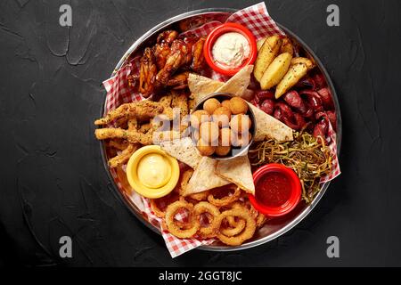 La piastra di birra con ali di pollo piccanti, anelli di calamari, patatine fritte anelli di cipolla, formaggio sfere, panate, salsa tartara e aglio Foto Stock