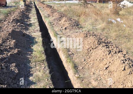 Scavando una trincea. Lavori di terra, scavo trincea. Trincea di terra lunga scavata per posare tubo o fibra ottica. Foto Stock