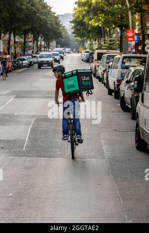 Berlino, Germania. 2 settembre 2021. Silvan, un autista per il servizio di consegna di cibo Uber mangia, si sposta in bicicletta con una scatola di trasporto sul retro su una strada nel quartiere Friedrichshain di Berlino. Credit: Carsten Koall/dpa/Alamy Live News Foto Stock