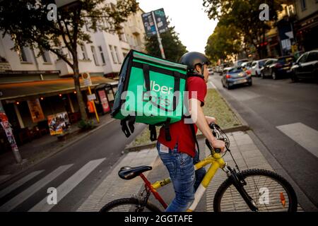 Berlino, Germania. 2 settembre 2021. Silvan, un autista per il servizio di consegna di cibo Uber mangia, si sposta in bicicletta con una scatola di trasporto sul retro su una strada nel quartiere Friedrichshain di Berlino. Credit: Carsten Koall/dpa/Alamy Live News Foto Stock