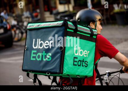 Berlino, Germania. 2 settembre 2021. Silvan, un autista per il servizio di consegna di cibo Uber mangia, si sposta in bicicletta con una scatola di trasporto sul retro su una strada nel quartiere Friedrichshain di Berlino. Credit: Carsten Koall/dpa/Alamy Live News Foto Stock