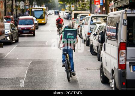 Berlino, Germania. 2 settembre 2021. Silvan, un autista per il servizio di consegna di cibo Uber mangia, si sposta in bicicletta con una scatola di trasporto sul retro su una strada nel quartiere Friedrichshain di Berlino. Credit: Carsten Koall/dpa/Alamy Live News Foto Stock