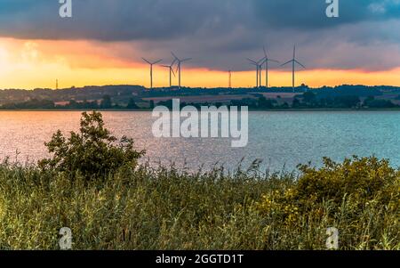 Wind farm su una collina sopra il lago all'alba, addensa sulle rive del lago in primo piano; Darłowo, Polonia, Mar Baltico Foto Stock