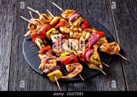 Gamberi Kabobs alla griglia con cipolla rossa, pepe dolce e ananas su un piatto di pietra nera Foto Stock