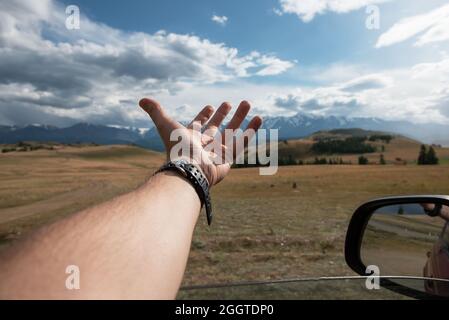 Primo piano del viaggiatore maschile mano in auto rilassante e godendo viaggio in auto in montagna Altai vacanza estiva e concetto di viaggio stradale. Foto Stock