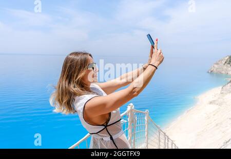 Bella donna di mezza età che prende selfie su smartphone mentre si trova in spiaggia durante l'estate. Foto Stock