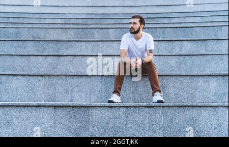 Uomo solitario sui gradini. Il ragazzo calmo in stile casual siede pensivo Foto Stock