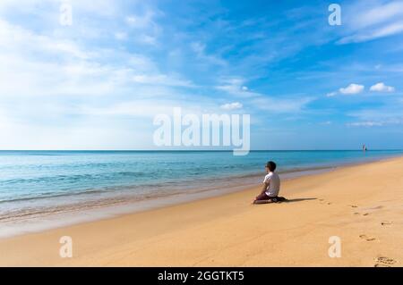 uomo solitario triste seduto su una bella spiaggia deserta e guardando in lontananza al mare Foto Stock