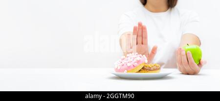 Donna su una dieta che fa una scelta fra alimento dolce della roba di rifiuto e frutta. Perdita di peso creativa e concetto di mangiare sano. Foto Stock