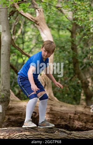 Ragazzo giovane gioia, sorpresa, esplorare, esercitarsi, arrampicare, climbering, equilibrando su un tronco caduto dell'albero nel bosco. Natura trovare e scoprire Foto Stock