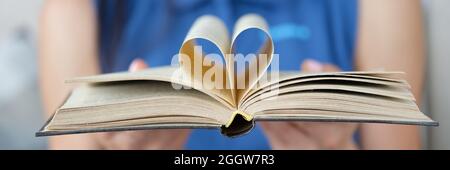 La donna sta tenendo il libro con una pagina in forma di cuore piegato nel centro Foto Stock