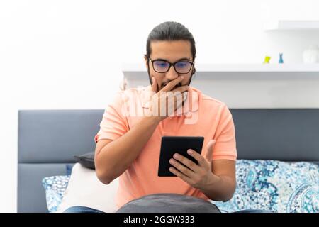 il giovane uomo sorprende mentre legge seduto a letto Foto Stock