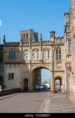 Wells St Andrew Street, vista in estate della gente in St Andrew Street che si avvicina alla casa di gatehouse medievale ad arco che conduce a Cathedral Green, Wells UK Foto Stock