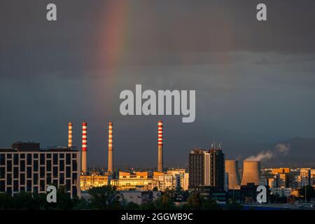 Camini centrali e arcobaleno luminoso contro il cielo scuro dopo la tempesta sopra il complesso industriale in ambiente urbano, Sofia, Bulgaria Foto Stock