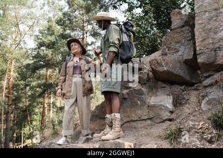 Donna anziana che tiene la mano del marito afroamericano vicino alle pietre nella foresta Foto Stock