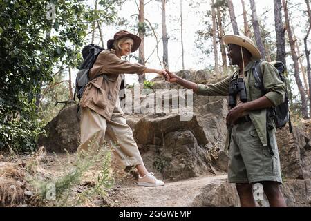 Escursionista afroamericano che tiene la mano di moglie anziana nella foresta Foto Stock