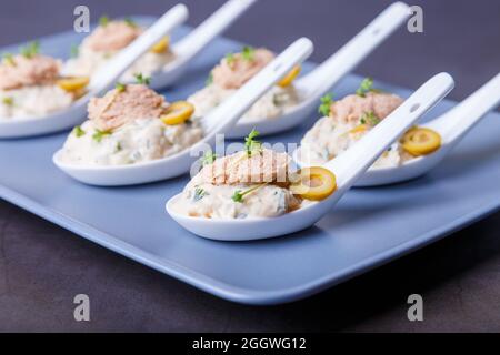 Antipasto freddo composto da fegato di merluzzo, caviale di merluzzo, olive, cetriolo e micrograni su cucchiai da servire. Piatto freddo tradizionale. Primo piano, piastra blu, nero Foto Stock