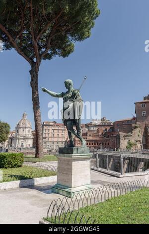 Statua in bronzo dell'imperatore romano di Augusto Cesare nella zona del Foro, Via dei fori Imperiali, Roma, Lazio, Italia. Antiche rovine sullo sfondo Foto Stock