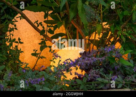 Sfere di pietra illuminate o palle illuminate di stile (primo piano) accoccolate in fioritura catmint - giardino paesaggistico al crepuscolo, Yorkshire, Inghilterra, Regno Unito. Foto Stock