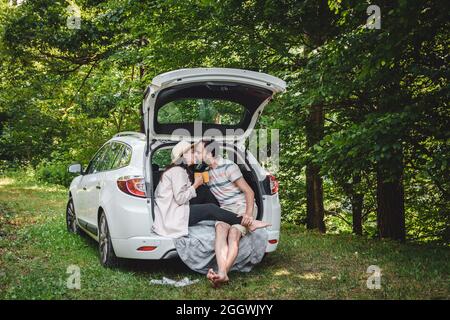 Felice coppia giovane su un viaggio in campeggio strada seduto in auto boot baciare. Foto Stock