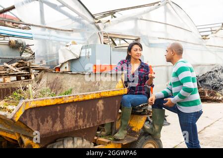 Donna contadina latino-americana che guida un camion mini dump, comunica con un collega maschio. Foto Stock