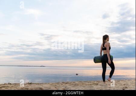 giovane modello fitness con materassino yoga al tramonto contro il cielo Foto Stock