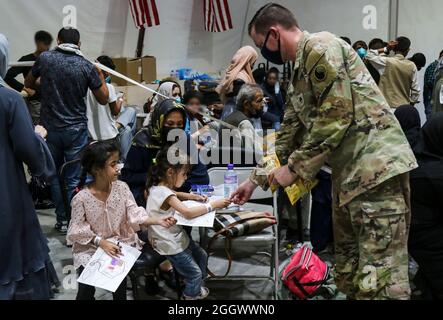 Un soldato della Guardia Nazionale dell'Esercito degli Stati Uniti assegnato alla Task Force Spartan, l'Esercito Centrale degli Stati Uniti offre caramelle ai bambini afghani evacuati mentre colorano mentre attendono le loro famiglie per completare il processo di arrivo in una struttura in Kuwait. I soldati USARCENT di tutte le componenti continuano ad abbracciare l'opportunità di sostenere le operazioni di evacuazione in Afghanistan con cura e compassione in luoghi in tutto il comando Centrale degli Stati Uniti. (STATI UNITI Esercito foto di SPC. Juan Carlos Izquierdo) Foto Stock