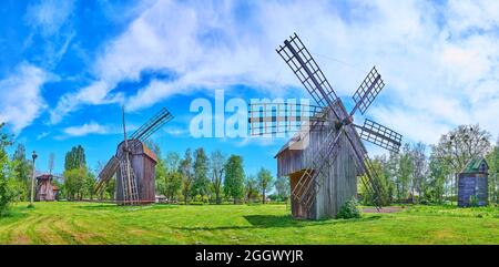 PEREIASLAV, UCRAINA - 22 MAGGIO 2021: Panorama del prato verde con vecchi mulini a vento in legno sotto il cielo azzurro, Pereiaslav Scansen, il 22 maggio in Foto Stock