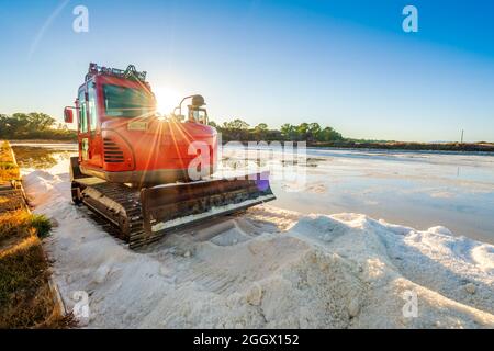 Bulldozer rosso che raccoglie il sale marino dallo stagno e che fa un mucchio di sale a salines a Faro, Algarve, Portogallo Foto Stock