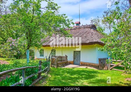 PEREIASLAV, UCRAINA - 22 MAGGIO 2021: Tradizionale casa hata villaggio imbiancato a calce con tetto di paglia, circondato da giardino primaverile fiorente, Pereiaslav Foto Stock